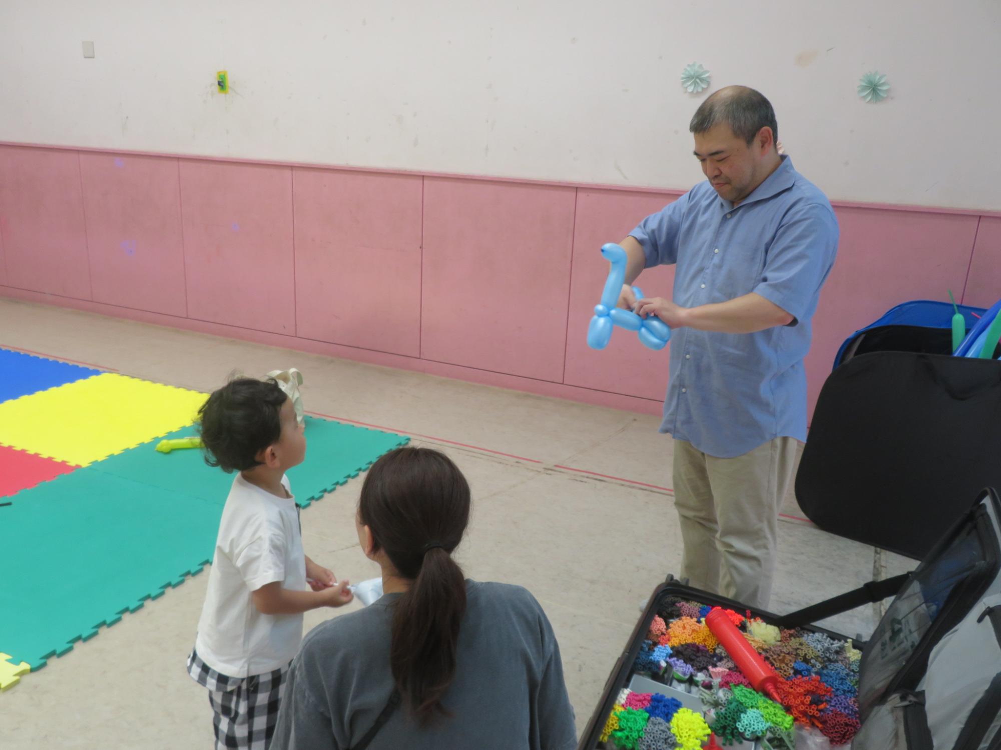 講師がバルーンで恐竜を作っているとことをみている幼児親子