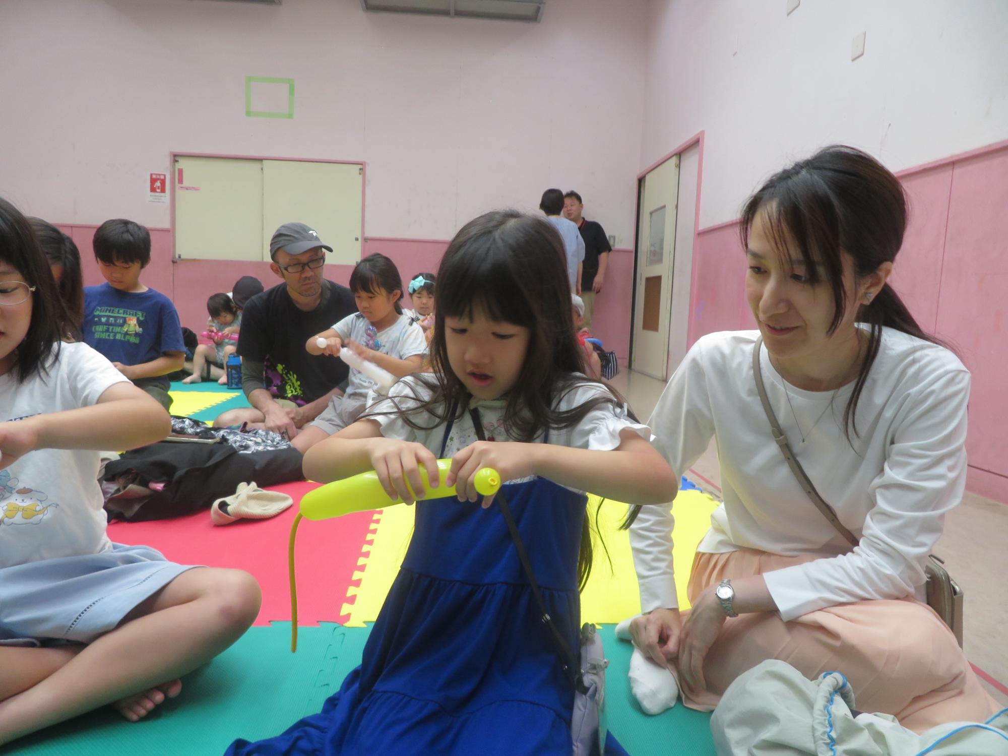 バルーンでジャンピングねずみを一生懸命作っている女の子と見守る母の様子