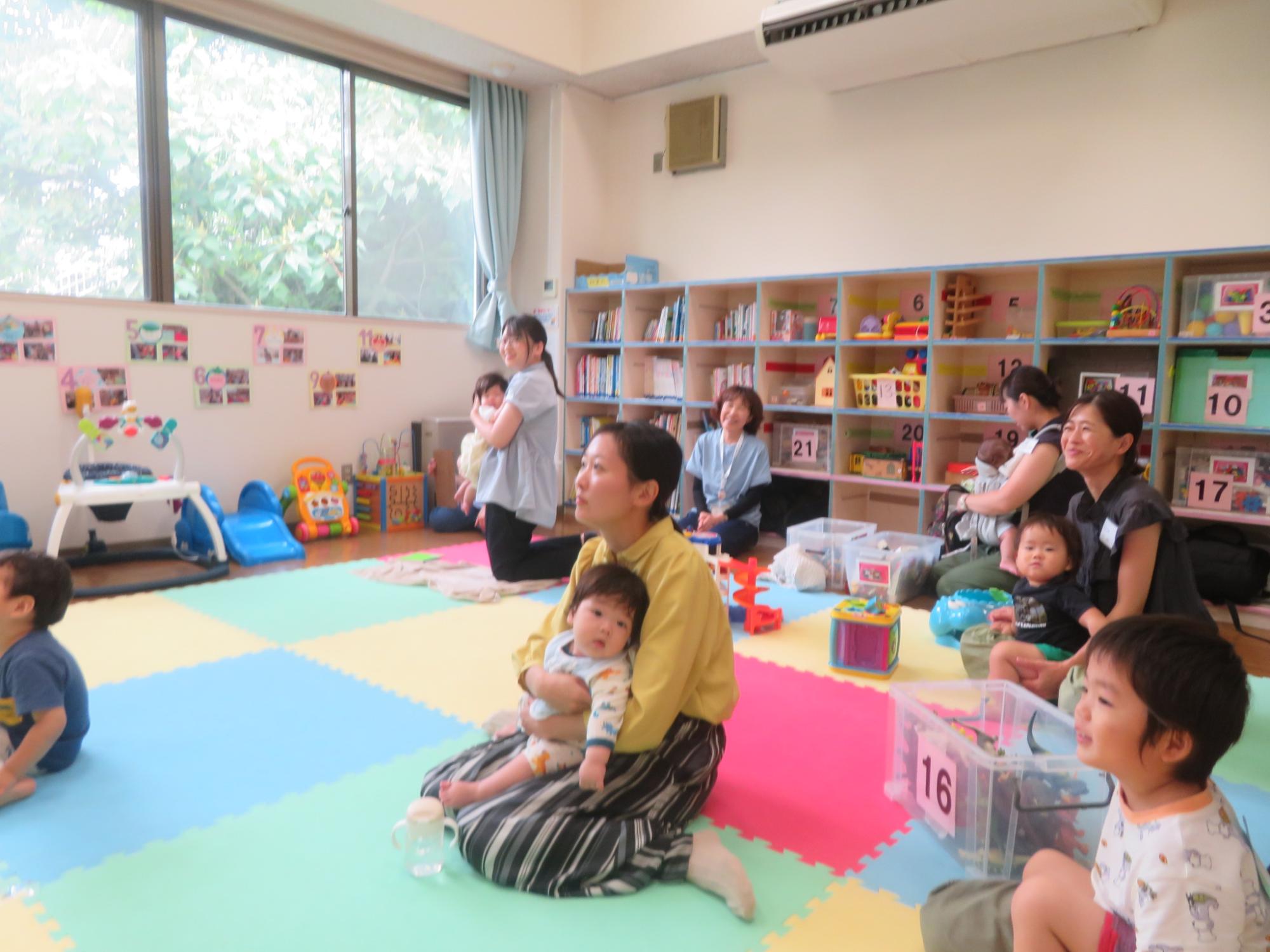 マットの敷かれた部屋で乳幼児を膝に乗せながらお話しする4人の母親たちの写真