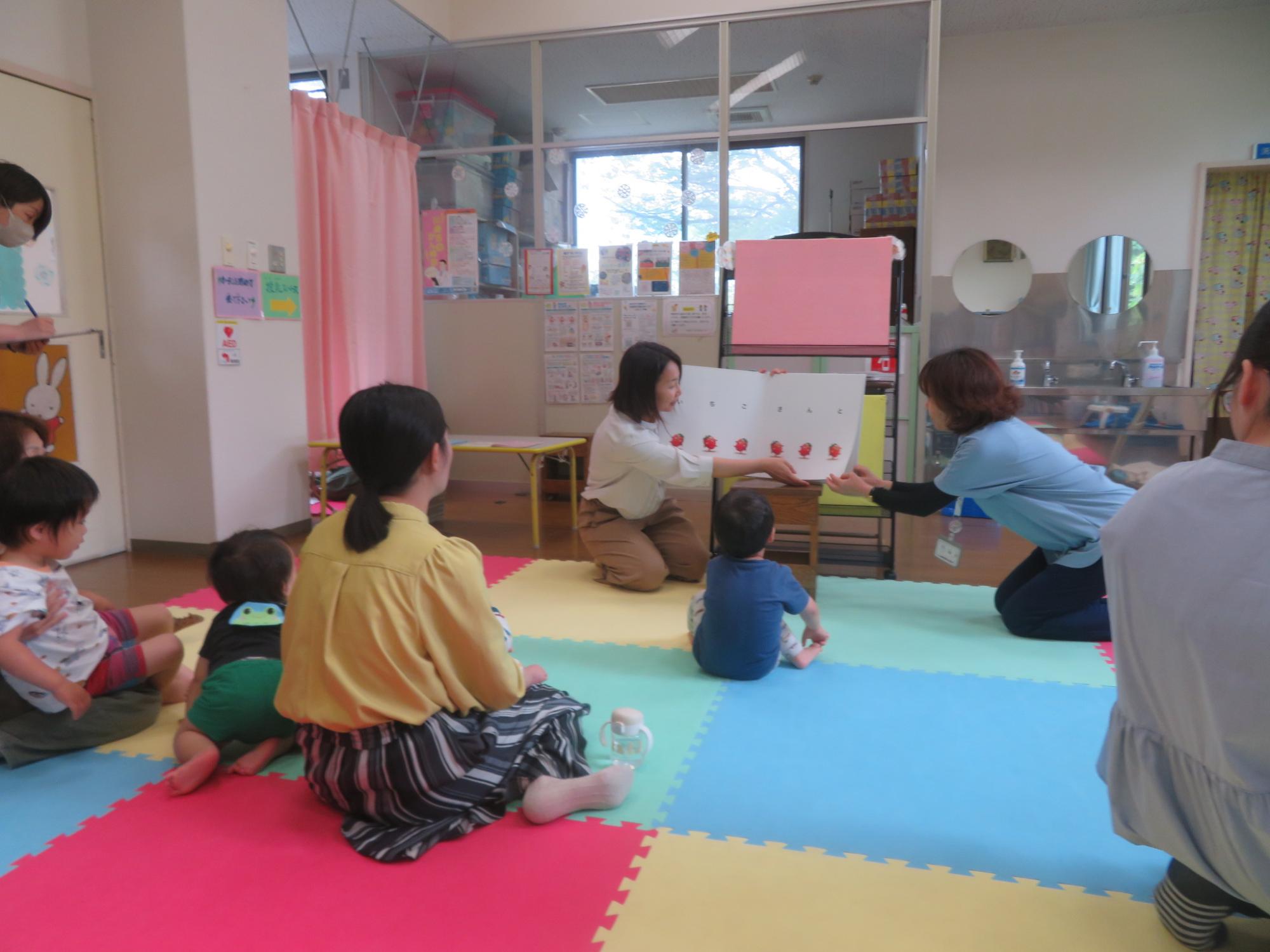 ボールを指で転がす母親と膝の上からボールを見る幼児の写真