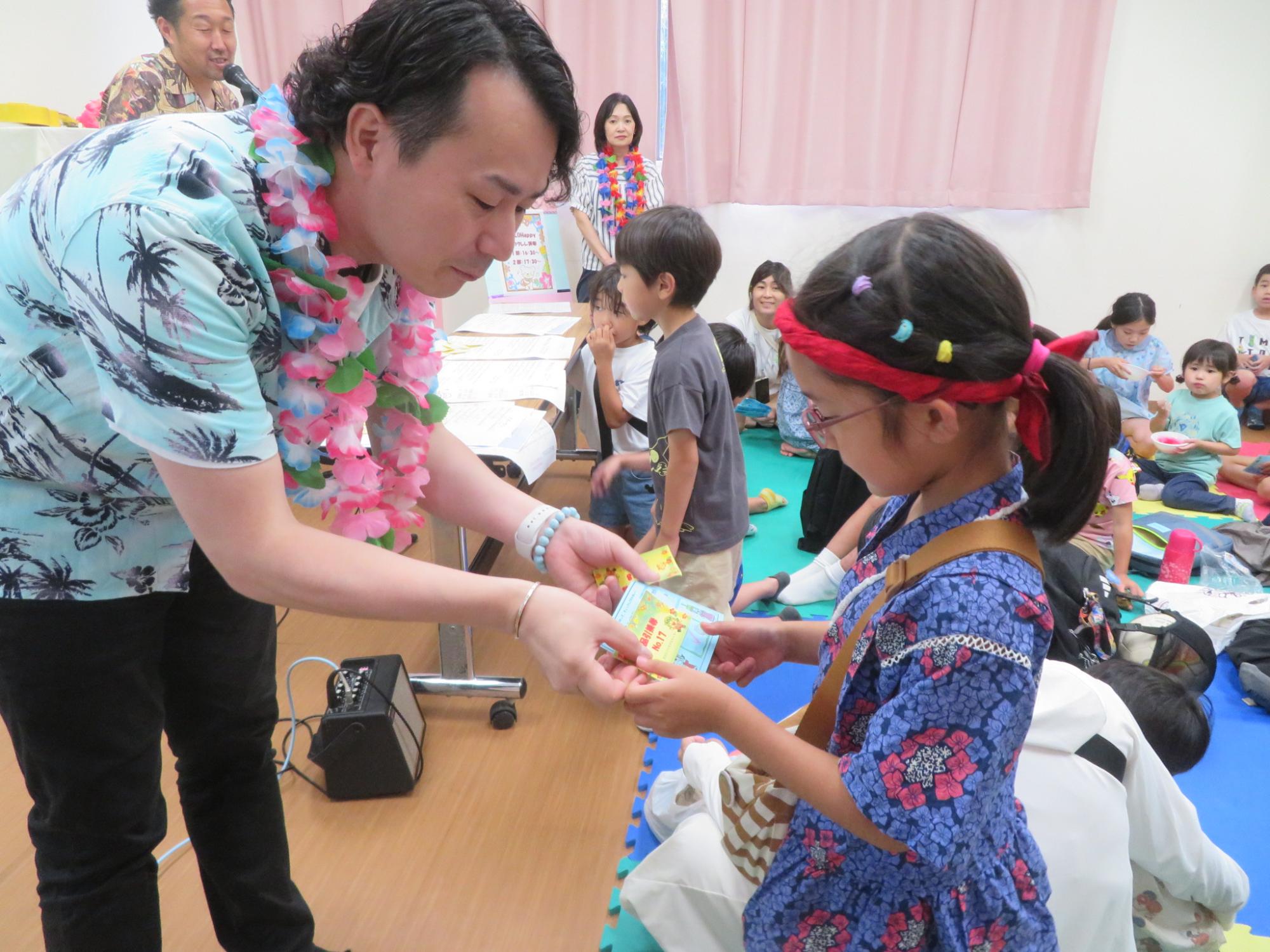 ゆりっこ夕涼みでアロハッピーの方から抽選会で景品引き換え券をもらっている女の子の写真