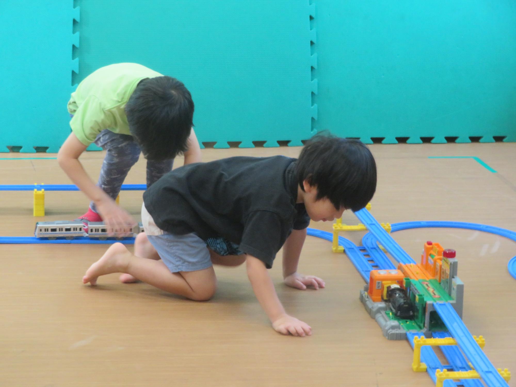 児童2名がプラレールのコースで電車を走らせて遊んでいる写真