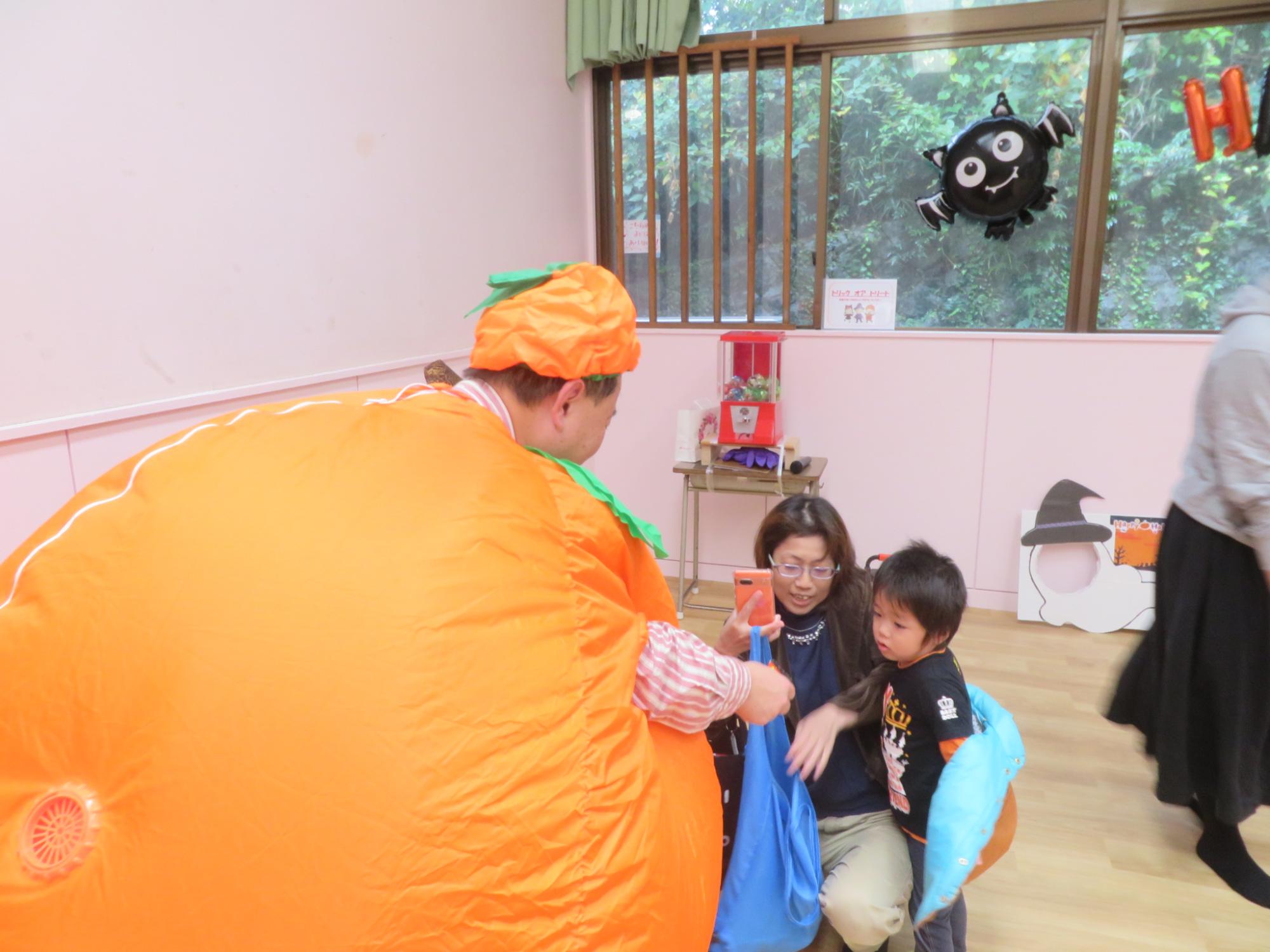 かぼちゃに仮装したスタッフが子どもたちにお菓子を配っている写真