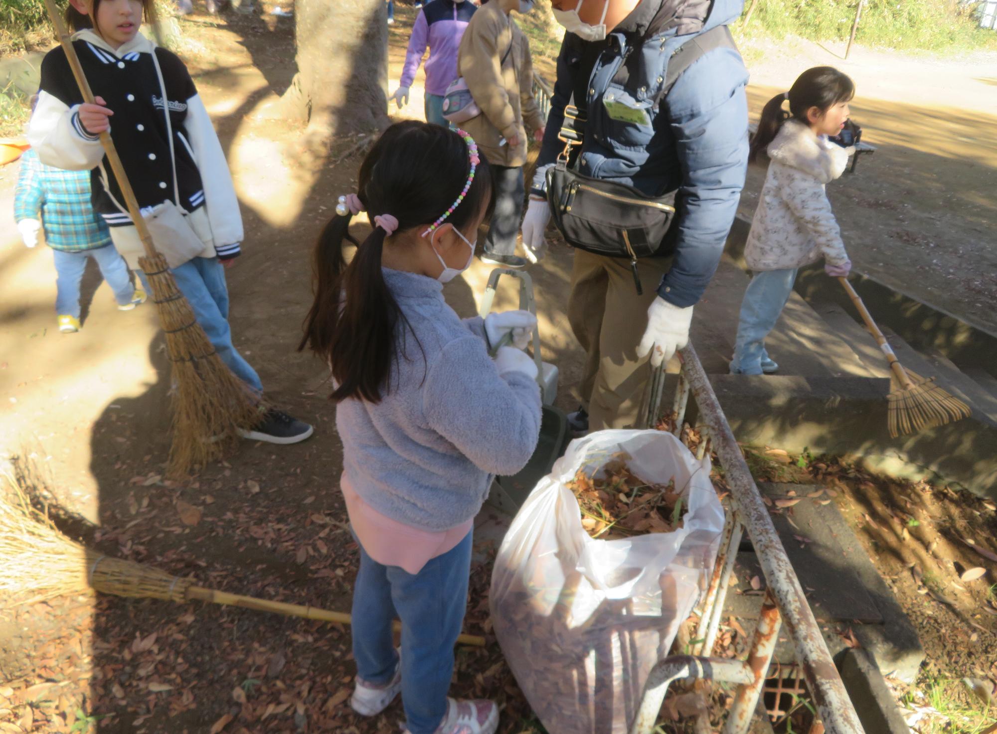 子ども達が楽しそうに落ち葉を集めている写真