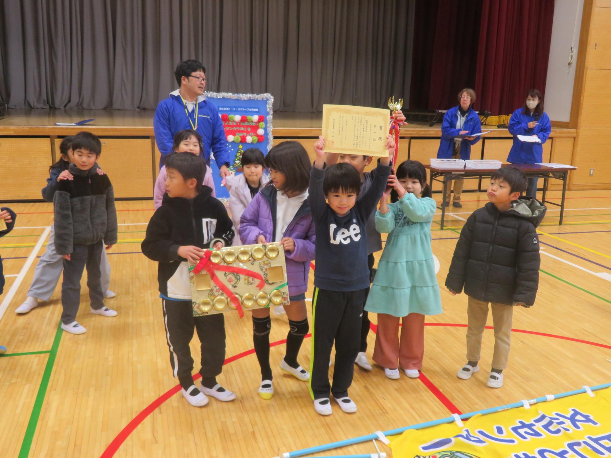 百合丘こども文化センター代表メンバーがトロフィー、表彰状、金のマンカラ台を持ってポーズ