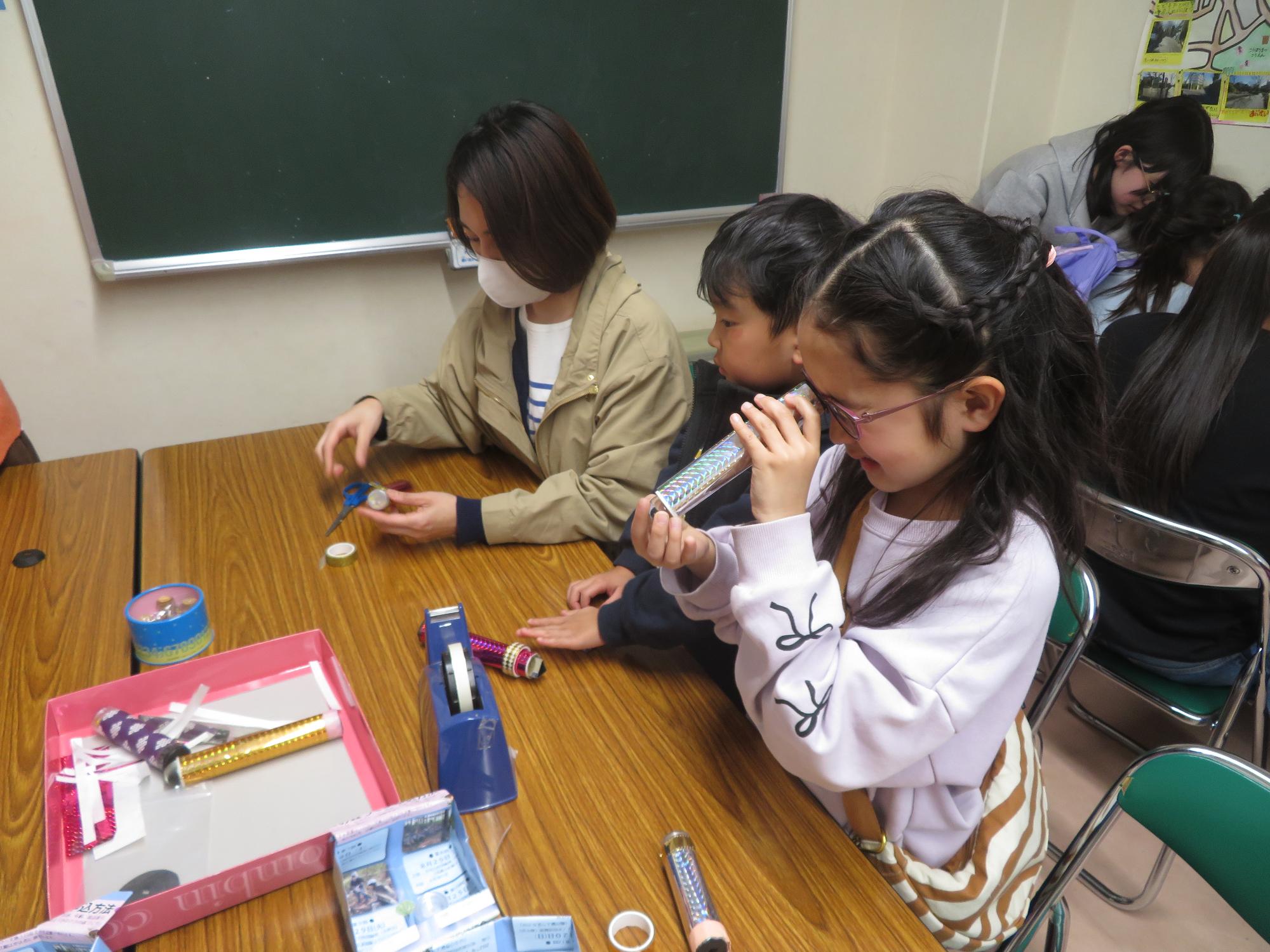万華鏡工作をしてる小学生と幼児親子の写真