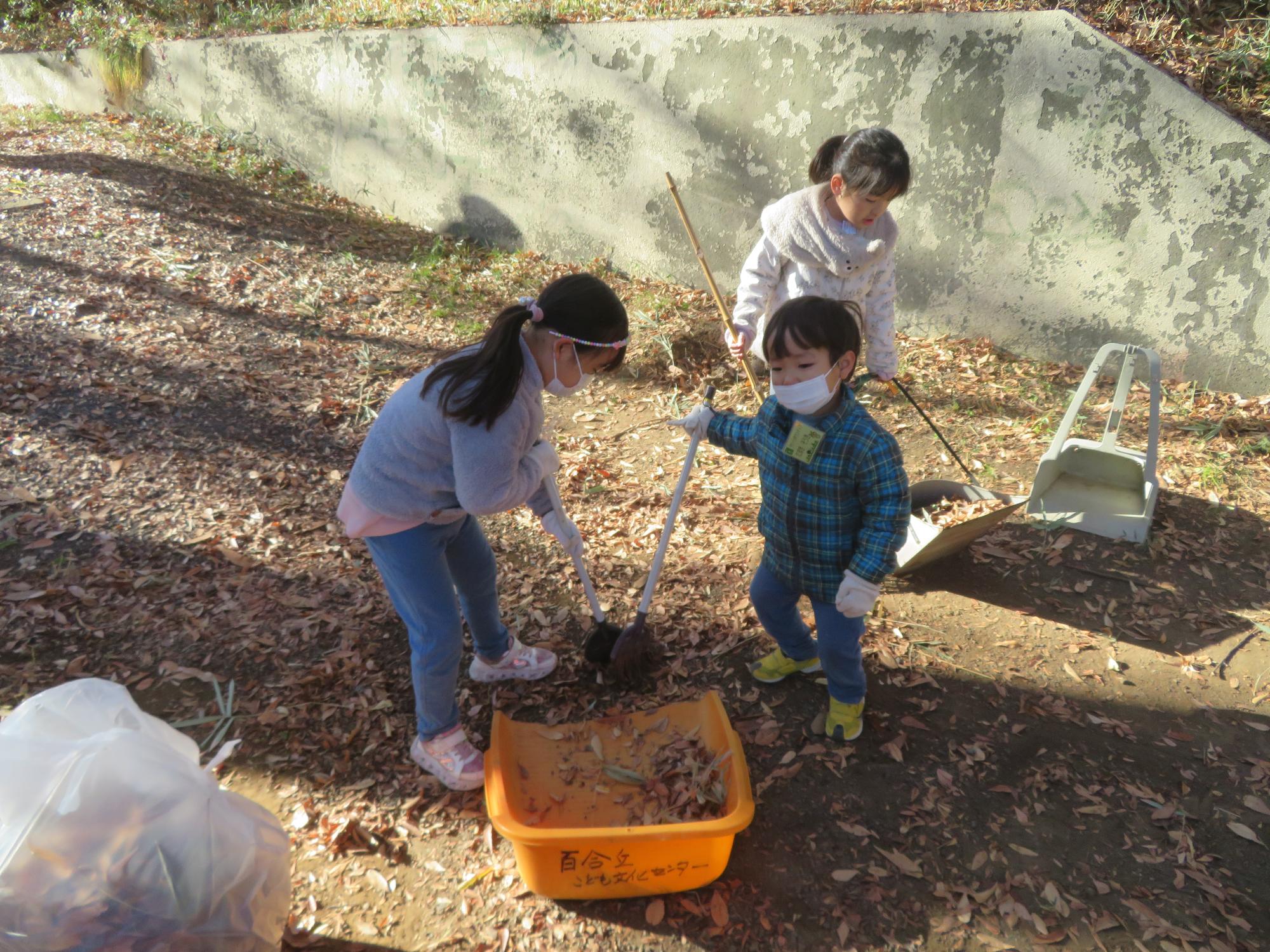 子ども達がほうきで落ち葉を集めている写真