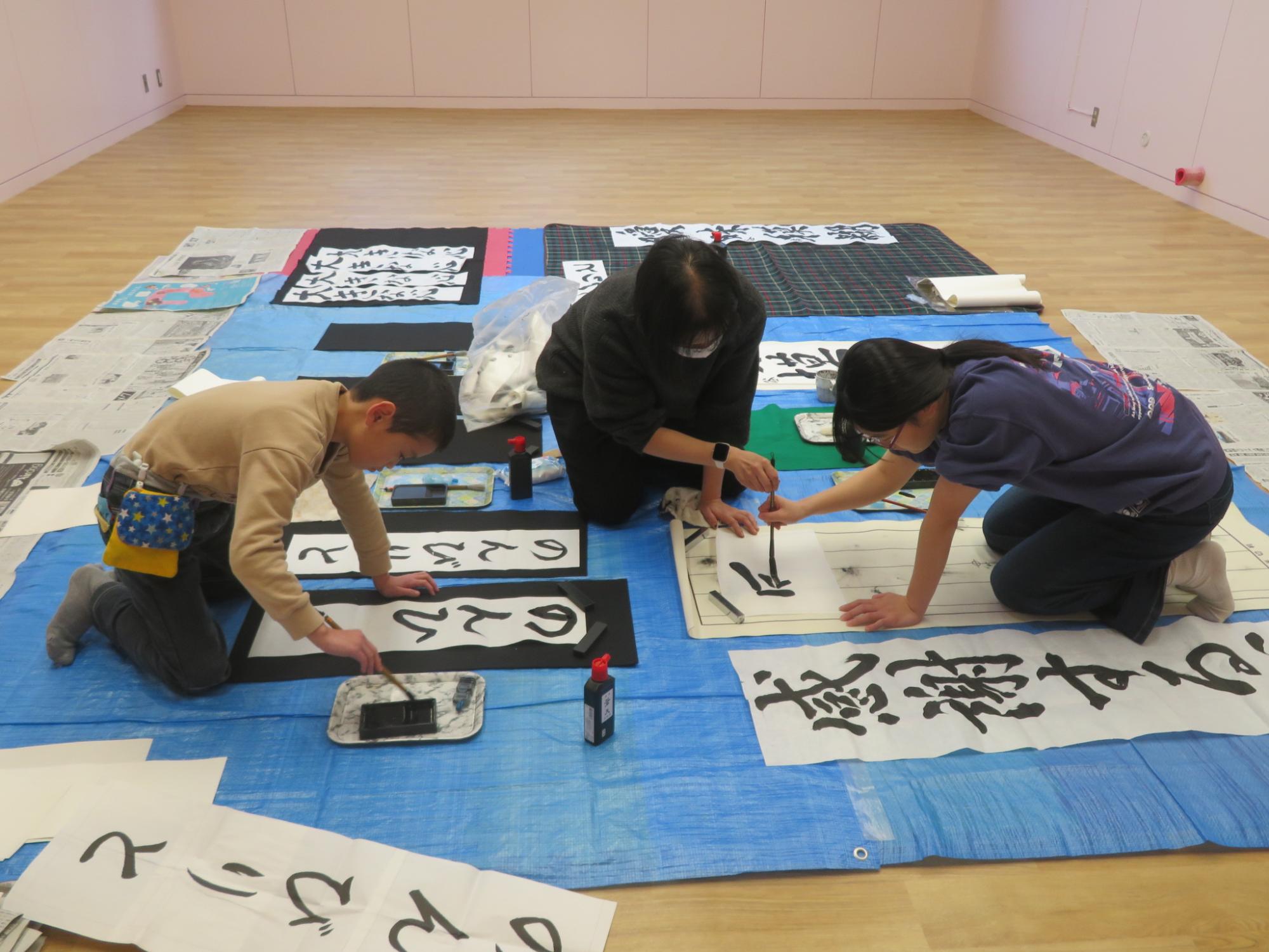 書道をする二人の児童と書き方を指導する講師の写真