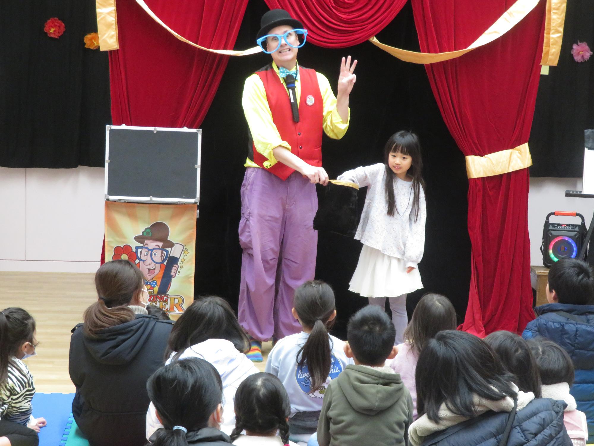 マジシャンの持つ帽子に手を入れる女の子の写真