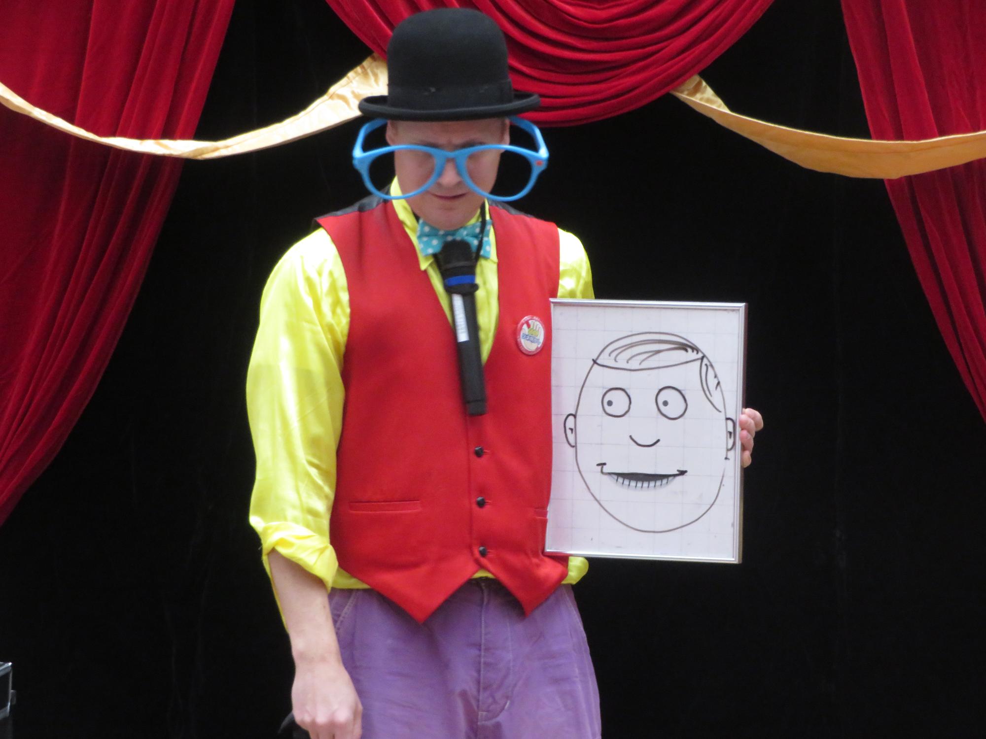 ホワイトボードに描いた顔の絵を参加者に見せるマジシャンの写真