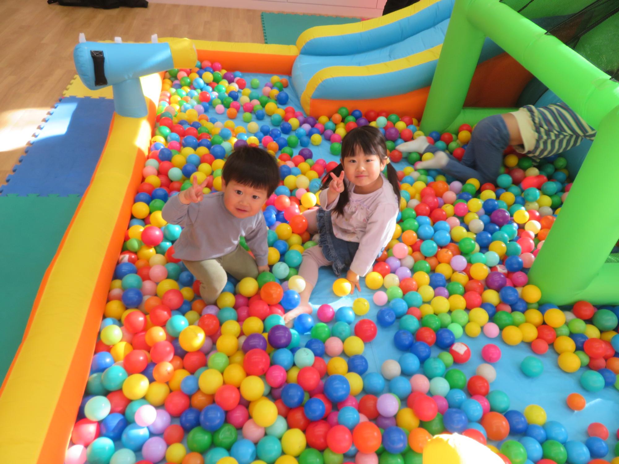 ボールプールの中でピースサインをする幼児の写真