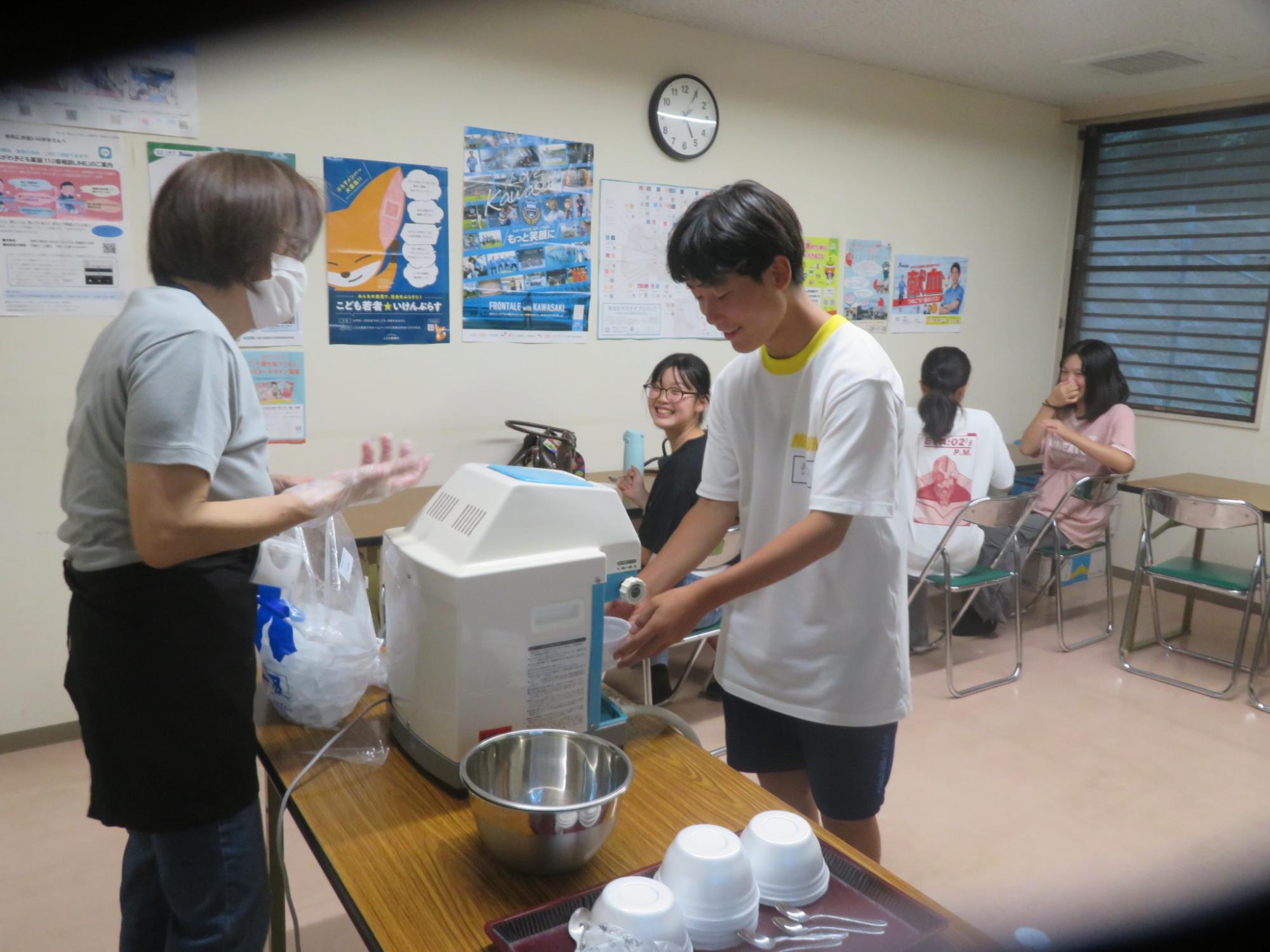 中学生男子がかき氷機でかき氷を削っている写真