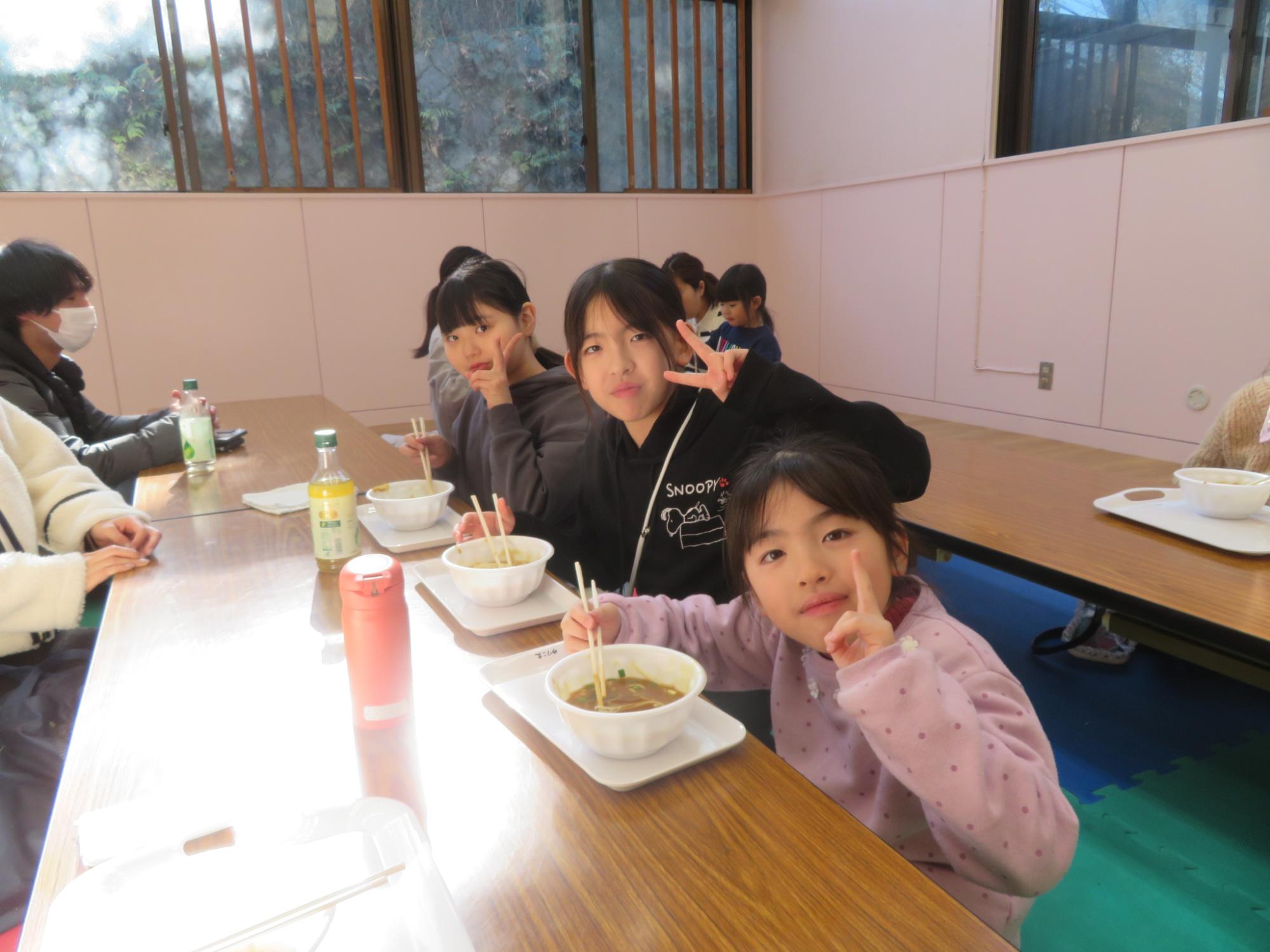 姉妹でピースサインをしながらうどんを食べている写真