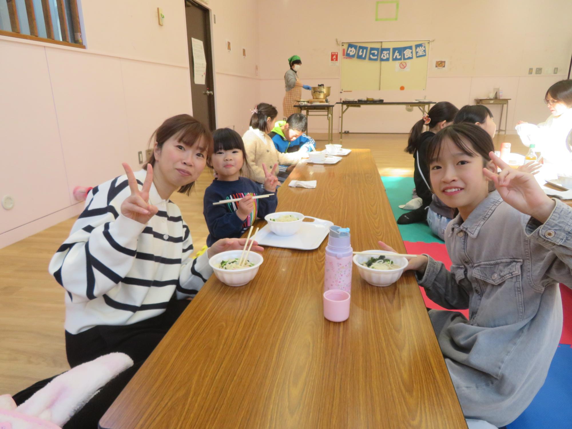 家族でピースサインをしながらうどんを食べている写真